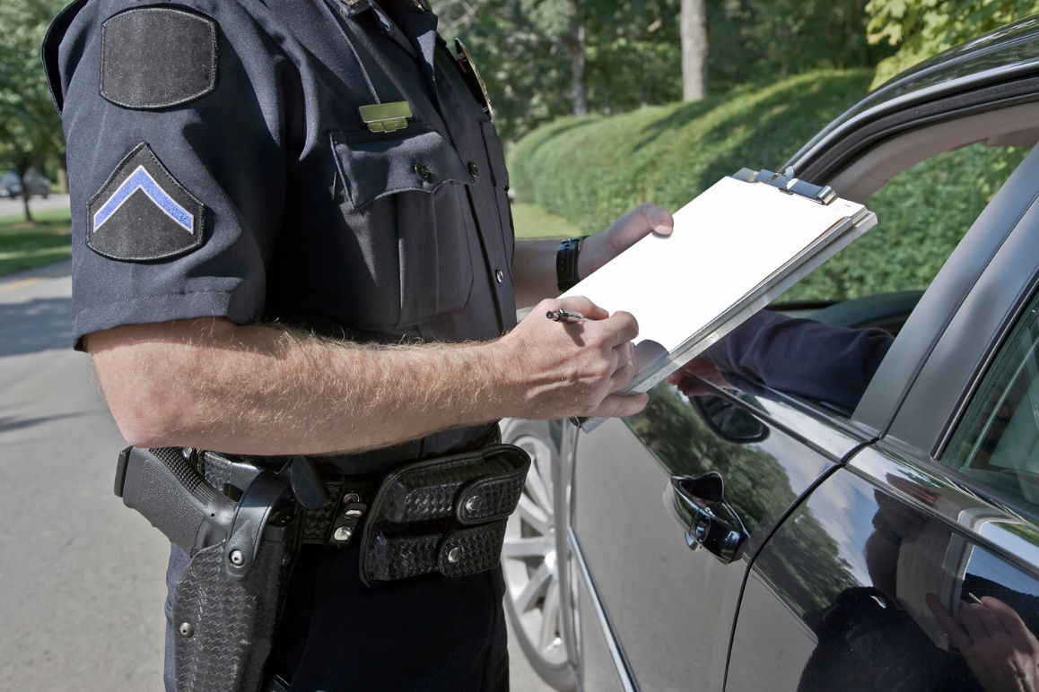 Police officer standing outside of a vehicle with the window rolled down writes on a clip board