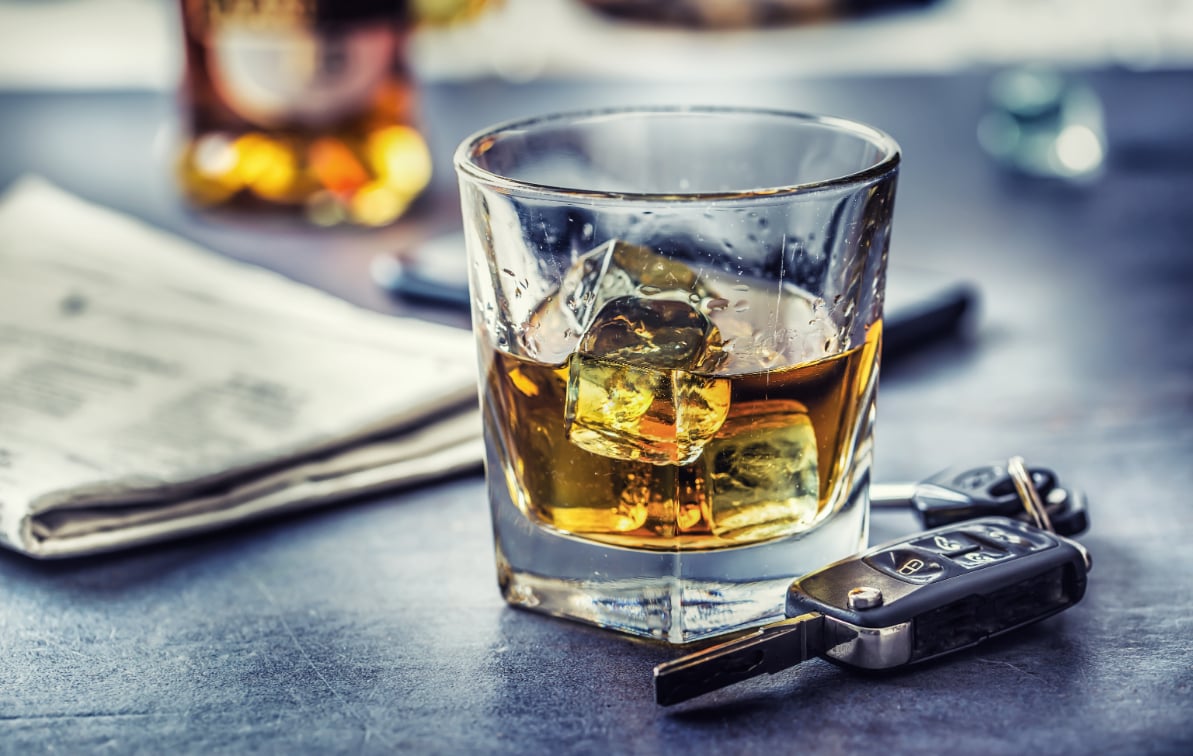 Shot glass with whiskey in it sitting on a table next to car keys