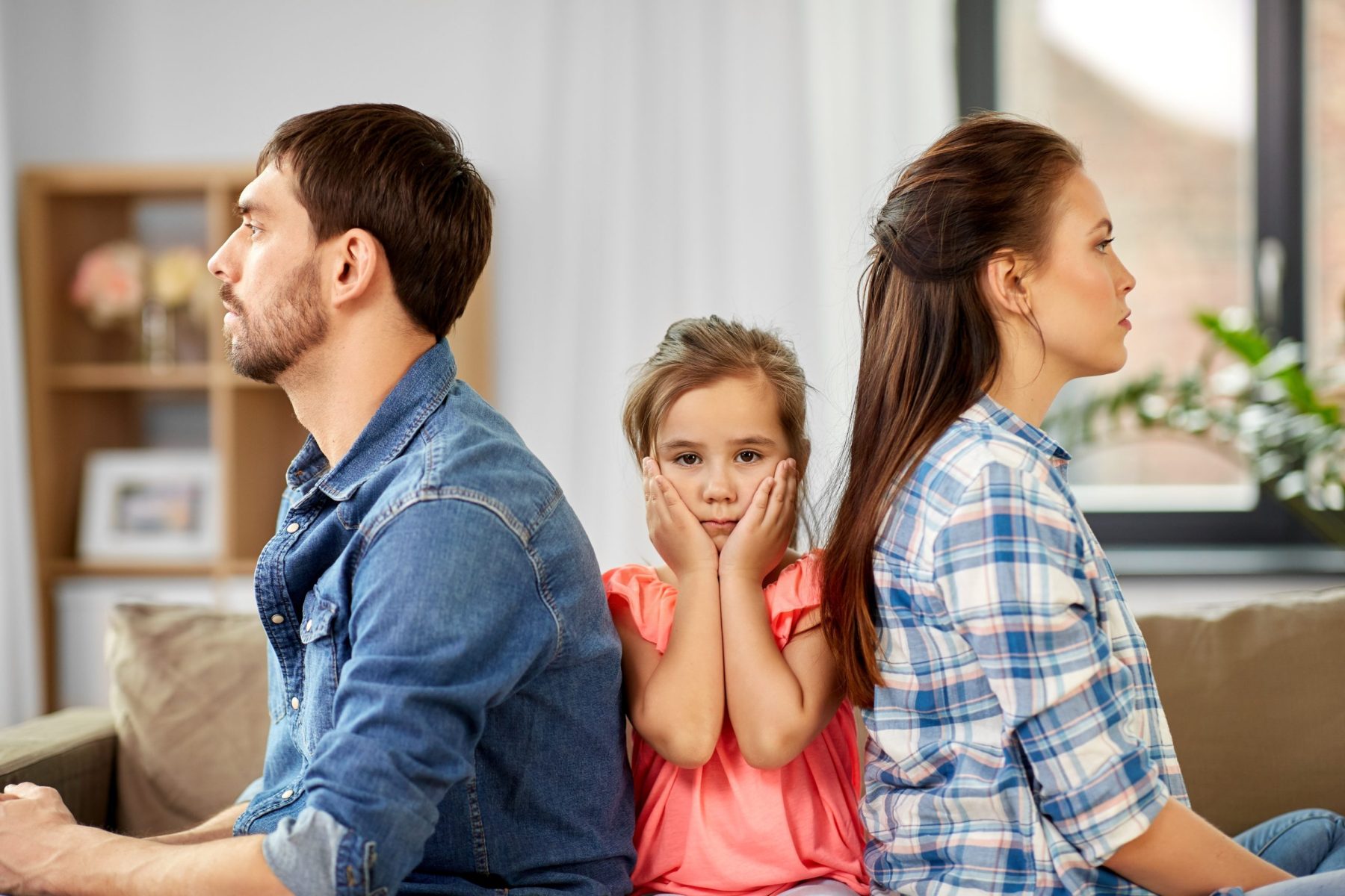 Man and woman with their backs to eachother, small girl on the middle with hands on face.