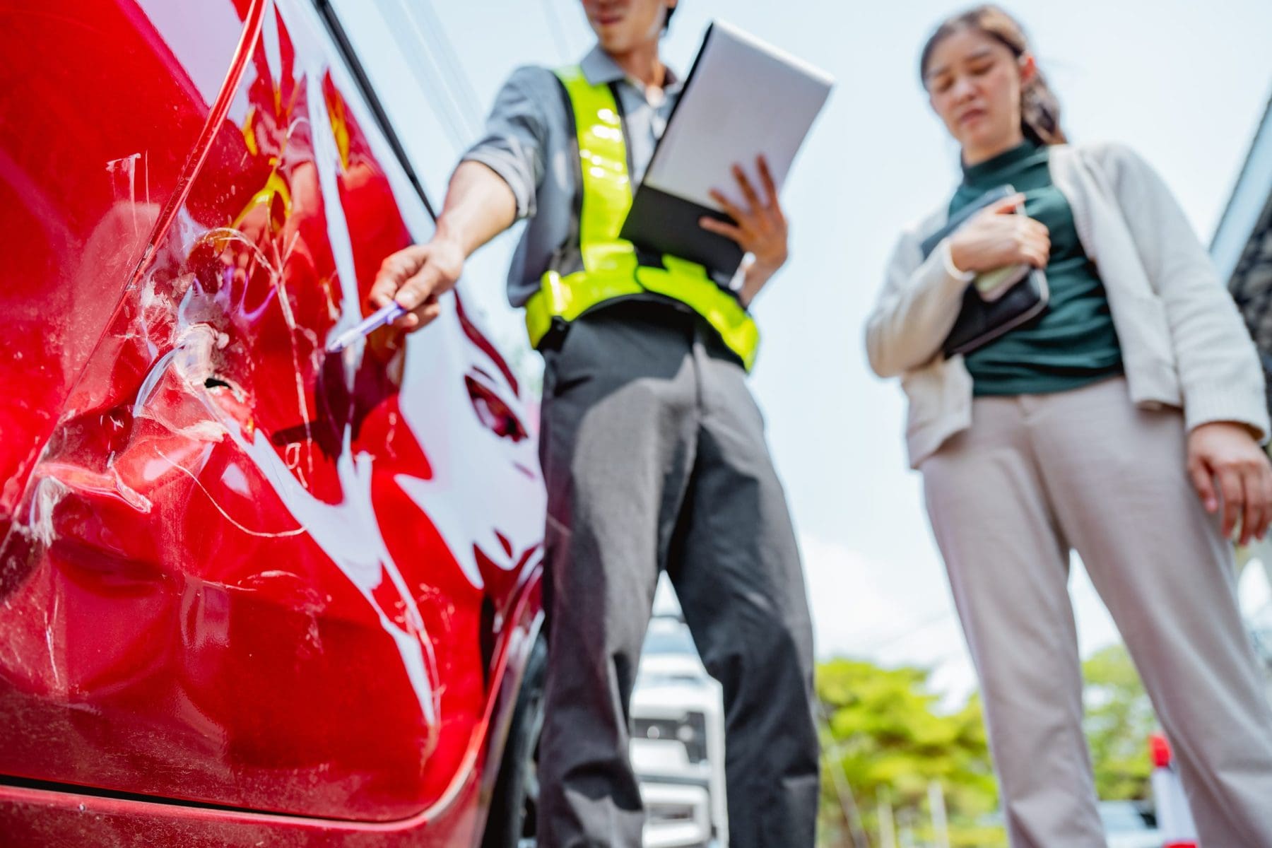 A man and a woman are examining a red car after crash.