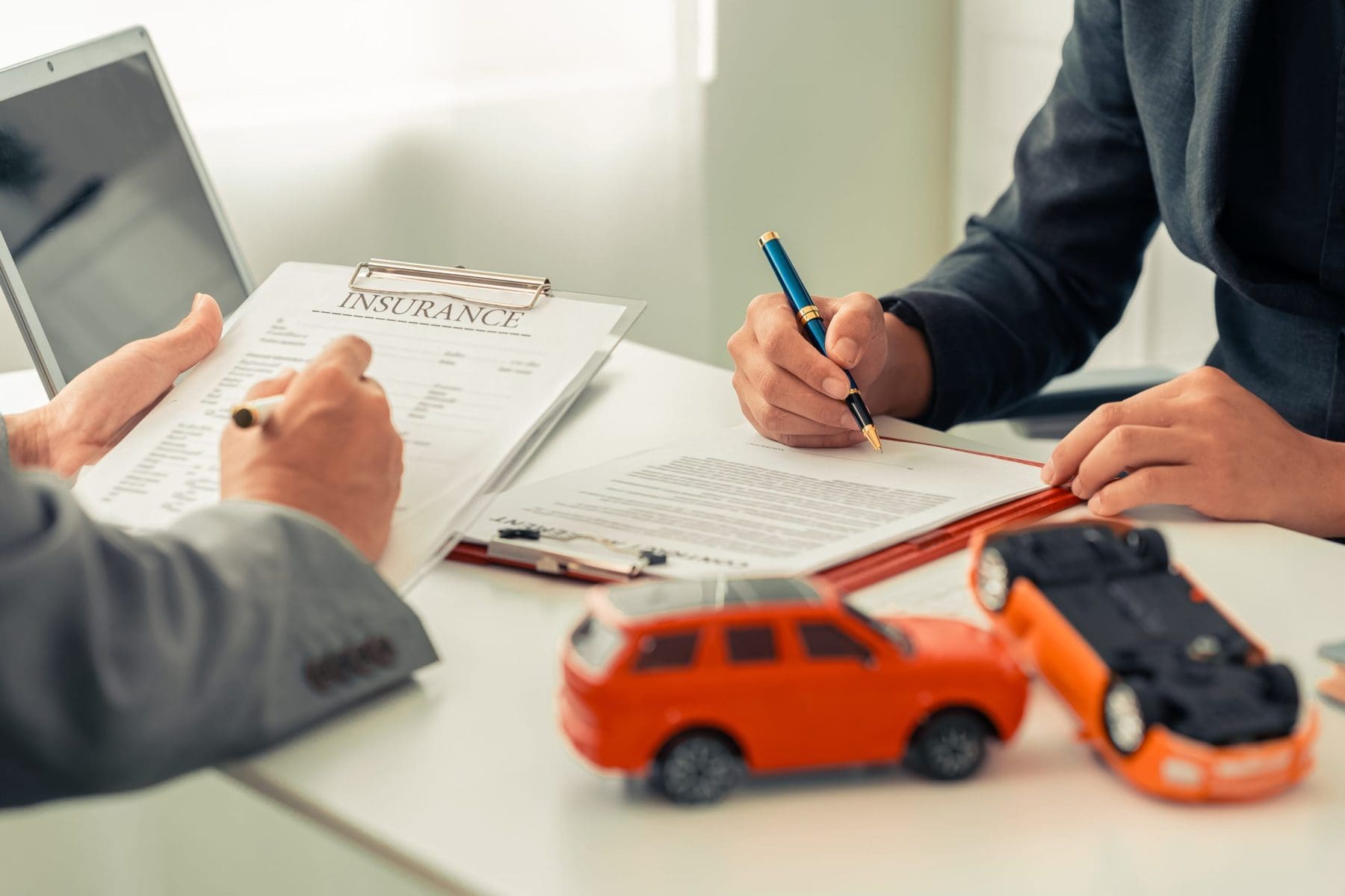 A small toy car model sits next to stacks of insurance documents, a calculator, and a pen on an office desk.