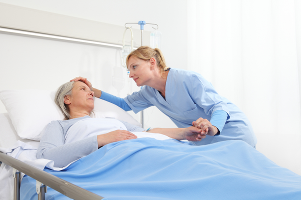 Elder woman laying in bed, nurse id holding her head.